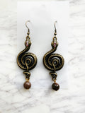 Pair of ornate winding serpent shape earrings, antique bronze tone with vintage crystals and Indian Agate beads on a marble background