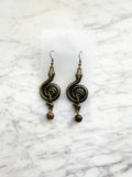 Pair of ornate winding serpent shape earrings, antique bronze tone with vintage crystals and Indian Agate beads on a marble background