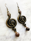 Pair of ornate winding serpent shape earrings, antique bronze tone with vintage crystals and Indian Agate beads on a marble background