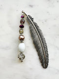 Tibetan silver feather bookmark adorned with bronze glass pearl, plum, and crystal beads handcrafted from repurposed vintage jewellery, displayed on a marble surface.