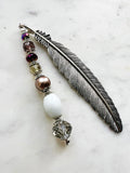 Tibetan silver feather bookmark adorned with bronze glass pearl, plum, and crystal beads handcrafted from repurposed vintage jewellery, displayed on a marble surface.