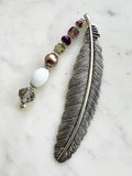 Tibetan silver feather bookmark adorned with bronze glass pearl, plum, and crystal beads handcrafted from repurposed vintage jewellery, displayed on a marble surface.