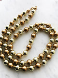 Vintage gold and bronze glass beaded flapper necklace laid on a white marble surface, featuring alternating reflective gold beads and matte bronze pearls with gold-tone spacers.