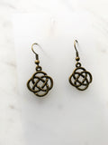 A pair of antique bronze Celtic knot dangle earrings on a white marble surface.