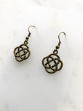 A pair of antique bronze Celtic knot dangle earrings on a white marble background.