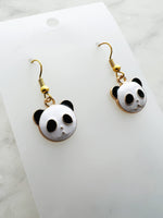 Panda-shaped earrings on a white card with marble background