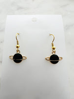 Black planet-shaped earrings with rings on a white marble surface