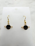 Black planet-shaped earrings with rings on a white marble surface