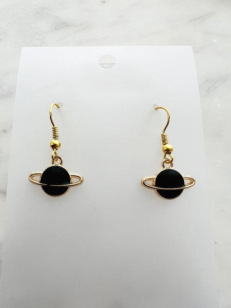 Black planet-shaped earrings with rings on a white marble surface