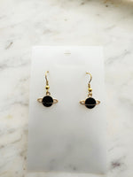 Black planet-shaped earrings with rings on a white marble surface