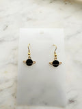 Black planet-shaped earrings with rings on a white marble surface