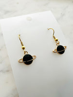 Black planet-shaped earrings with rings on a white marble surface