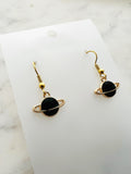 Black planet-shaped earrings with rings on a white marble surface