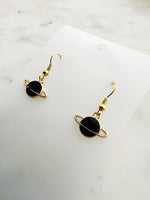 Black planet-shaped earrings with rings on a white marble surface