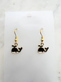 Kawaii Black whale-shaped earrings on a white card with a marble background