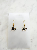 Kawaii Black whale-shaped earrings on a white card with a marble background