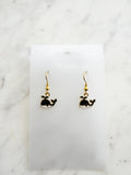 Kawaii Black whale-shaped earrings on a white card with a marble background
