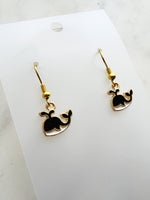 Kawaii Black whale-shaped earrings on a white card with a marble background