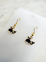 Kawaii Black whale-shaped earrings on a white card with a marble background
