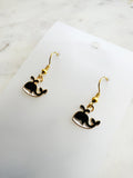 Kawaii Black whale-shaped earrings on a white card with a marble background