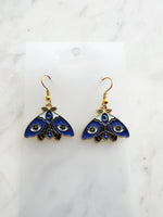 Kawaii Blue moth with evil eye earrings on a white marble background