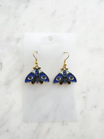 Kawaii Blue moth with evil eye earrings on a white marble background