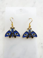 Kawaii Blue moth with evil eye earrings on a white marble background