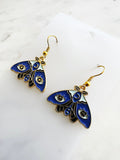 Kawaii Blue moth with evil eye earrings on a white marble background