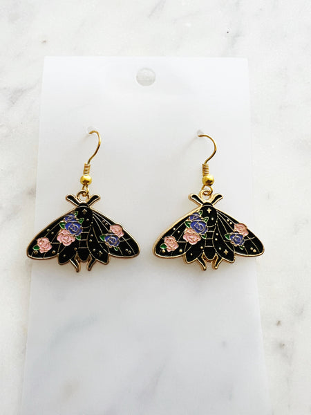 Kawaii Black moth-shaped earrings with floral details on a white card and a marble background