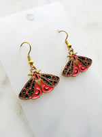 Kawaii Moth earrings on a white card with a white marble background
