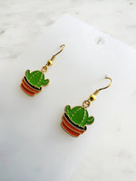 Kawaii Cactus-shaped earrings on a white card with a marble background