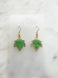 Maple leaf-shaped earrings on a white card with a marble surface