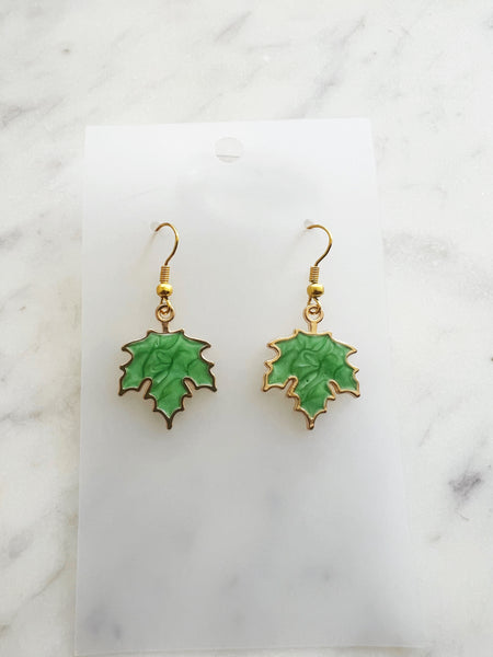 Maple leaf-shaped earrings on a white card with a marble surface