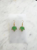 Maple leaf-shaped earrings on a white card with a marble surface