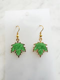 Maple leaf-shaped earrings on a white card with a marble surface