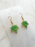 Maple leaf-shaped earrings on a white card with a marble surface