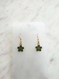 Green flower-shaped earrings on a white card with a marble background
