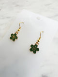 Green flower-shaped earrings on a white card with a marble background