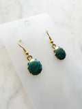 Teal earrings with gold hooks on a marble background