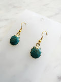 Teal earrings with gold hooks on a marble background