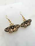 Enamel moth shaped earrings on a marble background