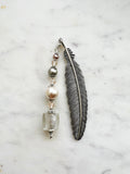 Handmade silver feather bookmark with neutral-toned repurposed vintage beads, including a clear foil glass cube, pearls, and crystals, displayed on a marble background.