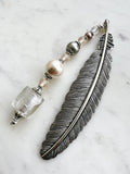 Side view of a Handmade silver feather bookmark with neutral-toned repurposed vintage beads, including a clear foil glass cube, pearls, and crystals, displayed on a marble background.