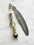 Side view of a Handmade feather bookmark with Tibetan silver feather and repurposed vintage beads in green, pearl, and crystal tones displayed on a marble background.