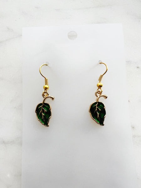 Pair of Kawaii green leaf-shaped earrings with gold hooks on a white card with marble background