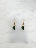Pair of Kawaii green leaf-shaped earrings with gold hooks on a white card with marble background