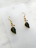 Pair of Kawaii green leaf-shaped earrings with gold hooks on a white card with marble background