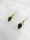 Pair of Kawaii green leaf-shaped earrings with gold hooks on a white card with marble background
