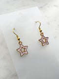 Star-shaped earrings on a white card with a marble background