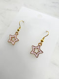 Star-shaped earrings on a white card with a marble background